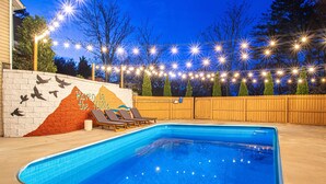 Una piscina con lettini, circondata da una recinzione in legno e luci decorative.