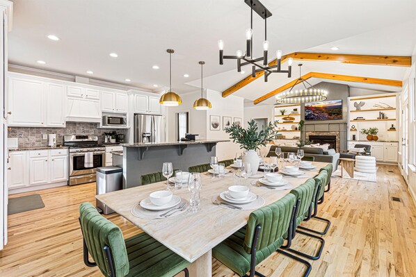 A modern kitchen with white cabinets, stainless steel appliances, and a dining area with a wooden table set for six. - Resort-style home w/ heated pool, hot tub, arcade (Fletcher)