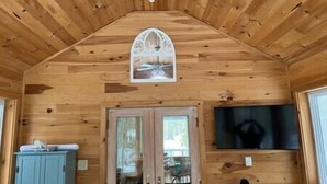 A wooden cabin interior with a pitched roof, a mounted picture, a television on the wall, and a door leading outside. - Create Memories only 10 min walk to Long Sands beach. (York)