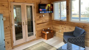 A cozy wooden cabin interior with a television mounted on the wall, a wicker sofa, and a glass table. - Create Memories only 10 min walk to Long Sands beach. (York)