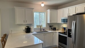 A modern kitchen with white cabinetry, a stainless steel refrigerator, a built-in oven, and a window providing natural light. - Create Memories only 10 min walk to Long Sands beach. (York)