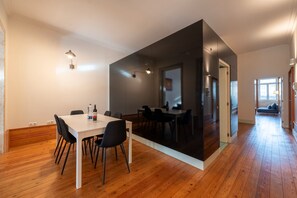 Un espace repas moderne avec une table blanche et des chaises noires, un plancher en bois et une cloison en verre.