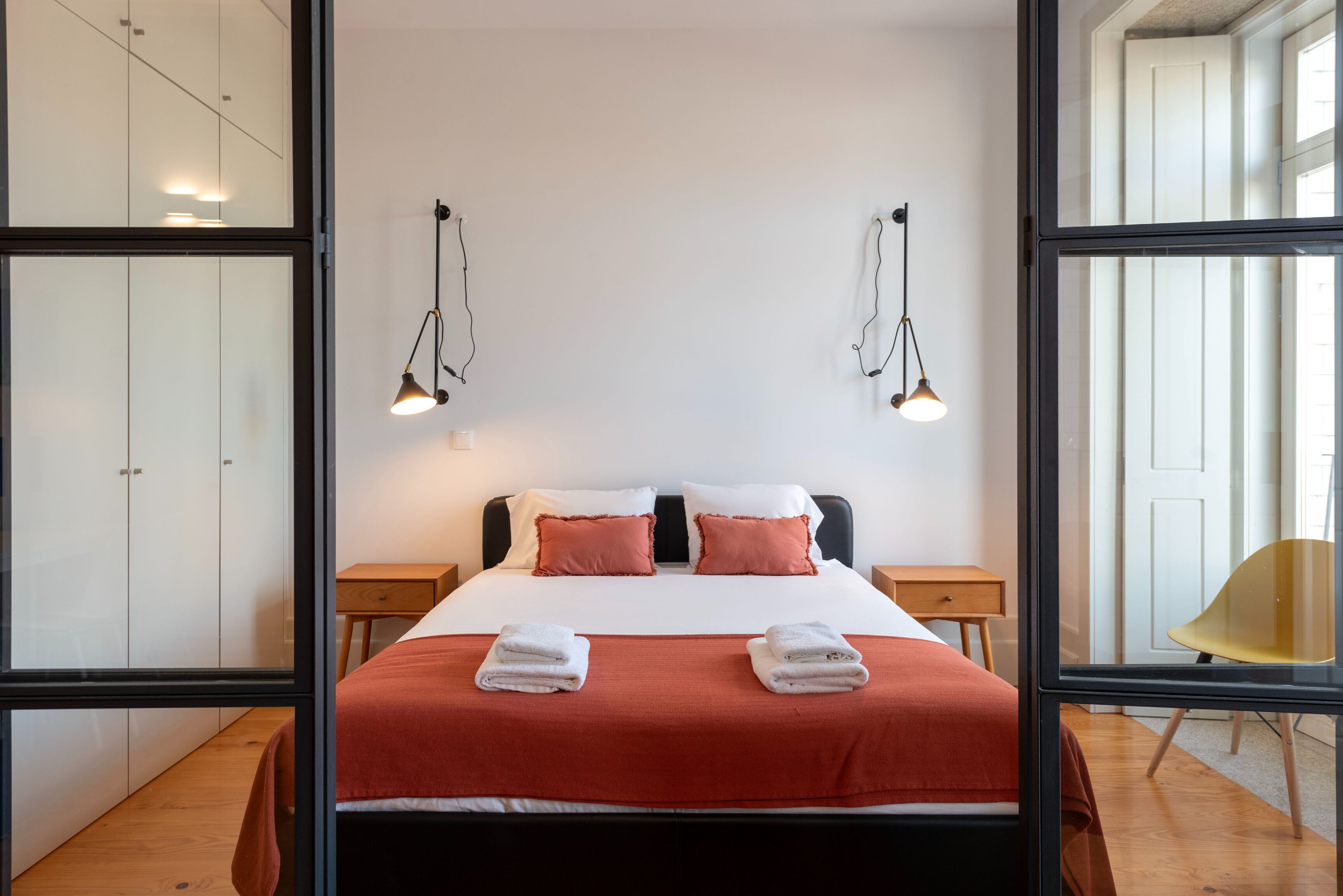 Una habitación de hotel moderna con una cama grande, dos mesitas de noche, piso de madera y un ventanal amplio.