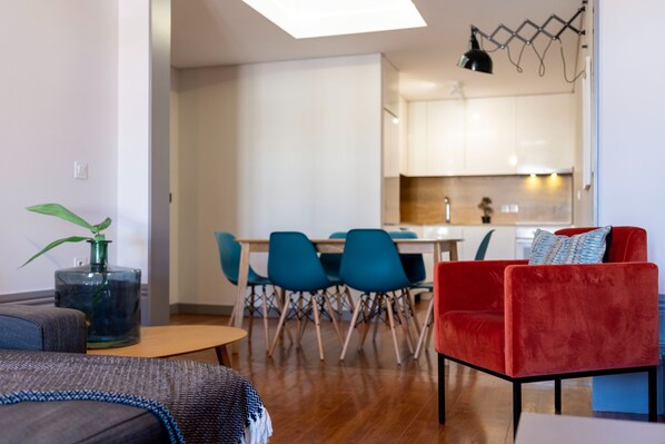 A modern living room with a sofa, a red chair, and a dining area with blue chairs.