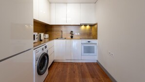 Cocina compacta con alacenas blancas, lavadora integrada, estufa y protector de salpicadero de madera.