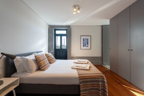 A modern bedroom with a large bed, a bedside table, a wardrobe, and a framed artwork on the wall.