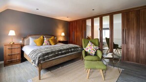 A bedroom with a bed, bedside lamps, a green armchair, a wooden wardrobe, and a view through a sliding door. - Amazing City Centre Home  (Derby)
