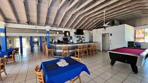 Un'ampia area interna con tavolo da biliardo, angolo bar con sgabelli e sala da pranzo con tavoli e sedie.