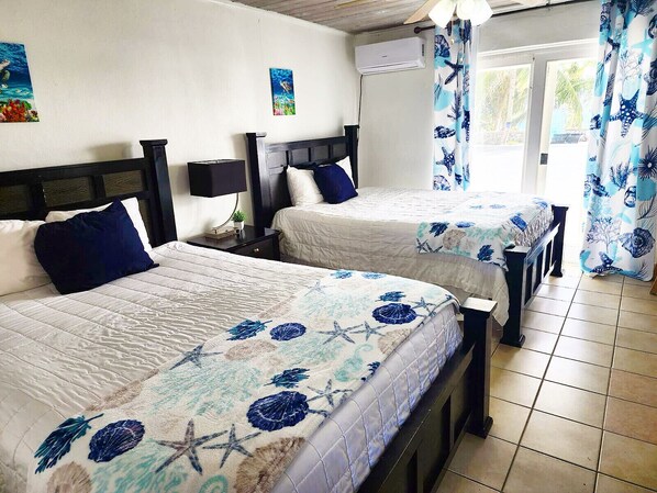 Une chambre d’hôtel avec deux lits, chacun recouvert d’une courtepointe à motifs floraux, une petite table de chevet avec une lampe et une fenêtre avec des rideaux.