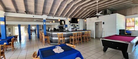 A spacious indoor area with a pool table, a bar area with stools, and a dining area with tables and chairs.