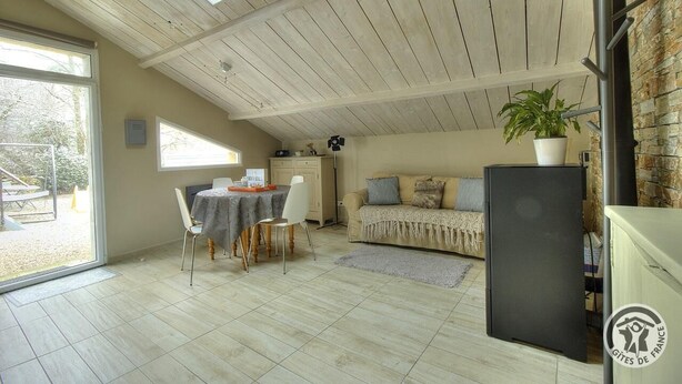 A cozy living room with a high ceiling, a dining area with a table and chairs, a sofa, a potted plant, and a black refrigerator.