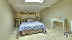 A bedroom with a skylight, a bed with patterned bedding, a nightstand, a desk, and a small rug.