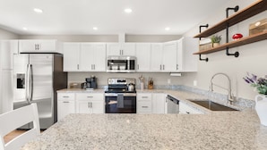 A modern kitchen with white cabinets, stainless steel appliances, granite countertops, and a built-in oven.