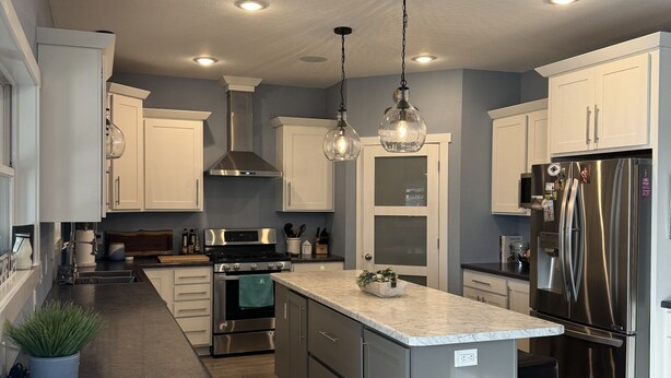 A modern kitchen with white cabinets, a marble countertop, stainless steel appliances, and pendant lighting.