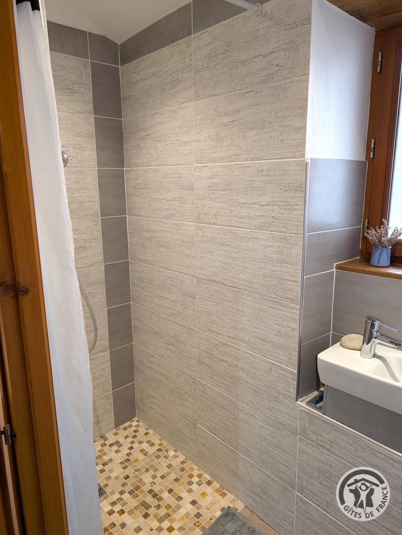 Un bagno con piastrelle grigie, zona doccia, lavandino e mobiletto in legno.