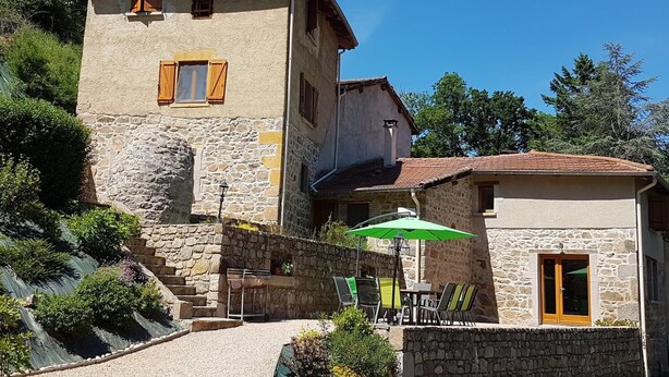 Un bâtiment en pierre doté d’un balcon et d’un patio aménagé avec des sièges extérieurs.