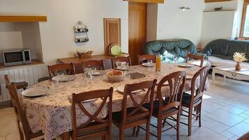 Een eetgedeelte met een tafel voor zes personen, omringd door houten stoelen, een magnetron, een houten kast en een groene gestoffeerde bank.