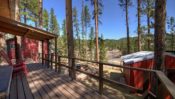 Une terrasse en bois avec une cabane rouge et un petit abri de jardin, le tout situé dans une zone boisée.