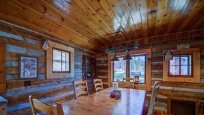 L’intérieur d’un chalet en bois, avec une grande table à manger, des chaises en bois et un luminaire suspendu.