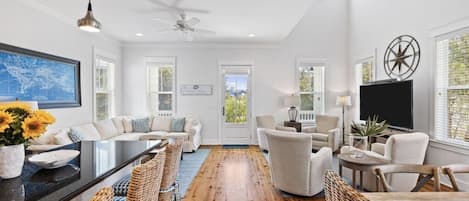 A spacious living room with a large sofa set, a dining table, wicker chairs, and a ceiling fan.