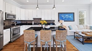 A modern kitchen with white cabinets, stainless steel appliances, and a central island with wicker chairs. - Sugar Blue, walk to the beach
 (Santa Rosa Beach)