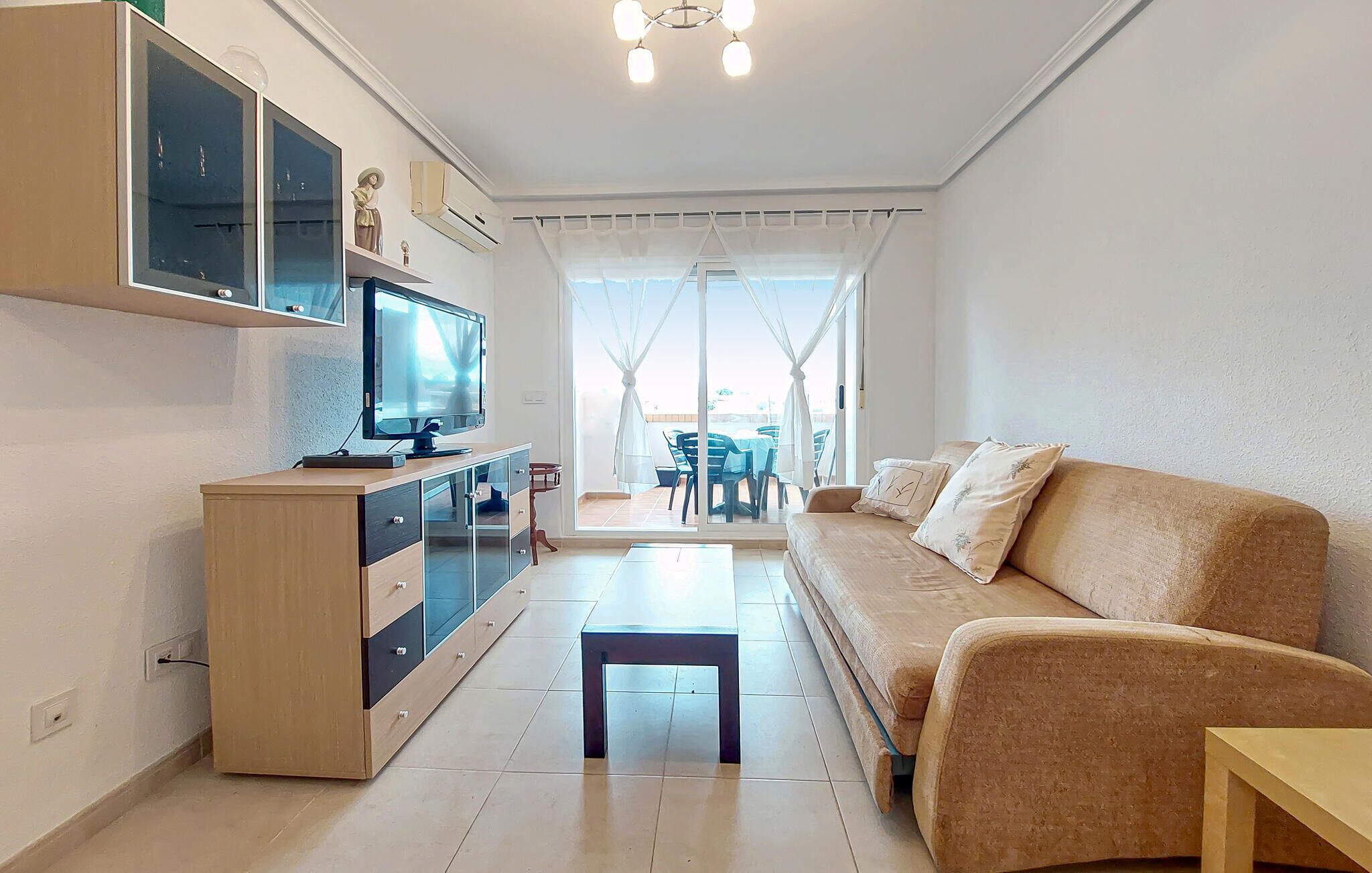 Ein modernes Wohnzimmer mit Sofa, Fernseher und einem Essbereich, der durch die Glastür sichtbar ist.