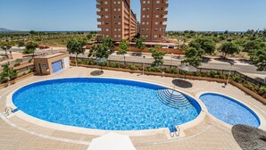 A swimming pool with a sunbathing area, surrounded by a landscaped garden, and adjacent to a multi-story building.