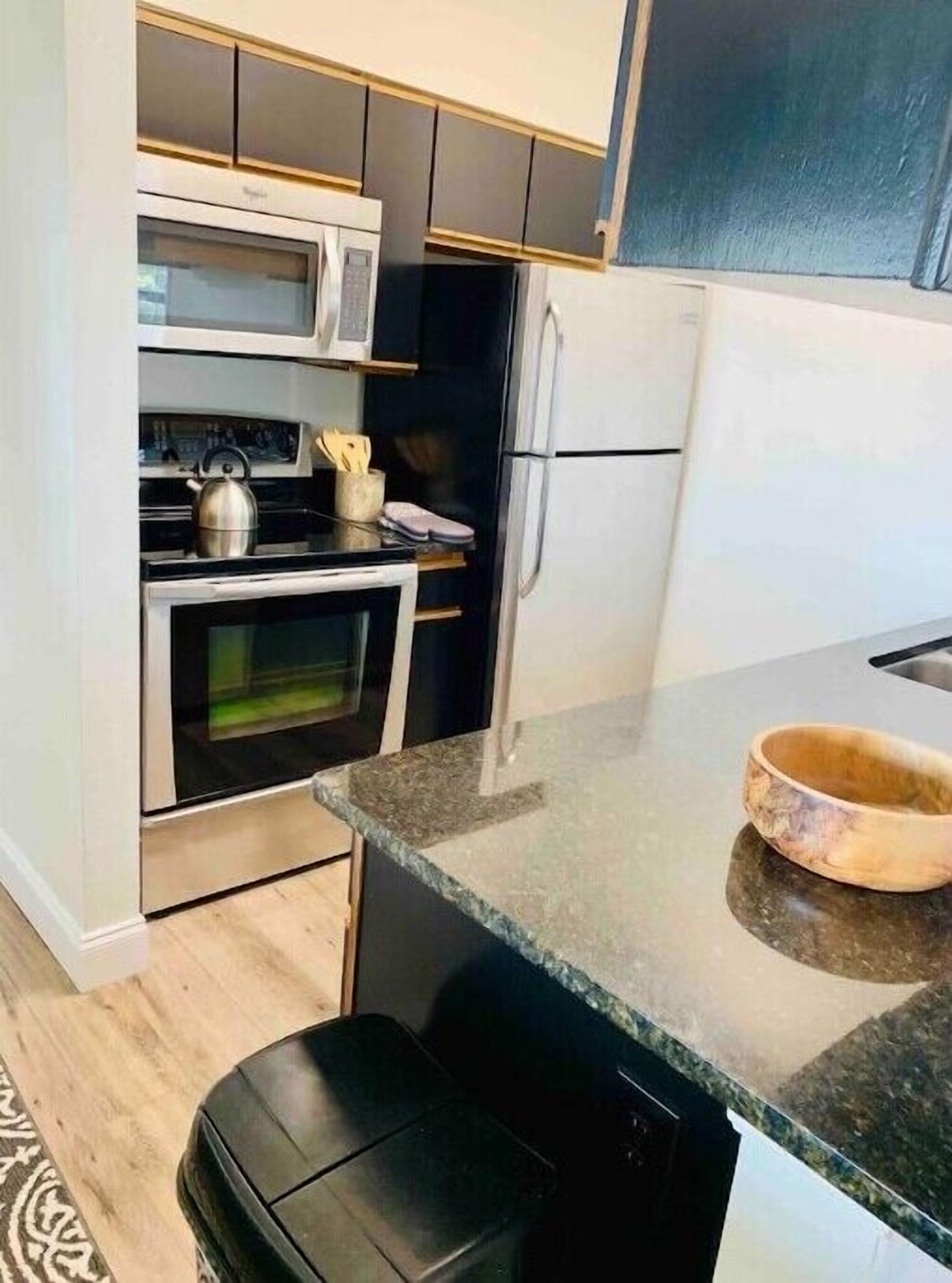 A modern kitchen with stainless steel appliances, a granite countertop, and a wooden bowl on the counter.