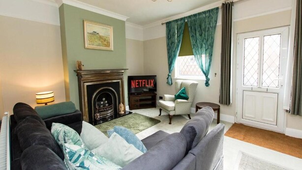A living room with a fireplace, a sofa, a chair, and a television displaying 'NETFLIX'. - Captivating 2-bed House in Chesterfield (Chesterfield)