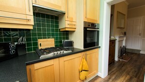 A kitchen with wooden cabinets, a gas stove, a microwave, and a green tiled backsplash. - Captivating 2-bed House in Chesterfield (Chesterfield)