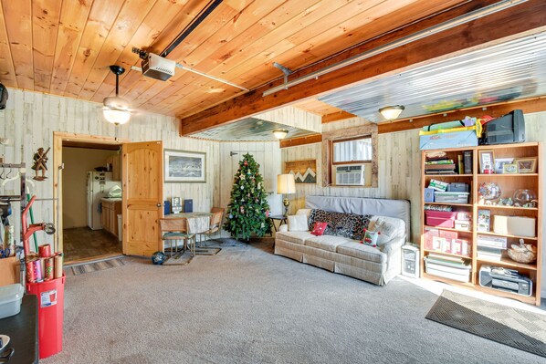 A cozy living room with a wooden ceiling, a Christmas tree, a sofa, and a bookshelf. - Rustic Jefferson Retreat w/ Fire Pit: Near Athens! (Jefferson)