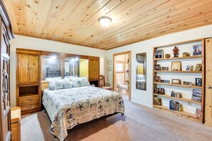 A bedroom with a wooden ceiling, a bed with a beach-themed bedspread, a wooden wardrobe, and a bookshelf with framed photos and books. - Rustic Jefferson Retreat w/ Fire Pit: Near Athens! (Jefferson)