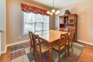 Une salle à manger avec une table et des chaises en bois, une fenêtre avec des stores, un lustre et un buffet en bois doté de portes en verre.