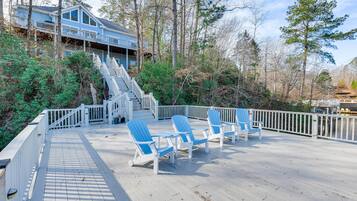 A wooden deck with blue Adirondack chairs and a staircase leading to a house.