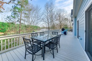 Une terrasse dotée d’une table et de chaises à plateau en verre, offrant une vue sur un plan d’eau et des arbres.