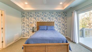 A bedroom with a wooden bed, a nightstand with a lamp, a window with a view of the outside, and a patterned wallpaper.