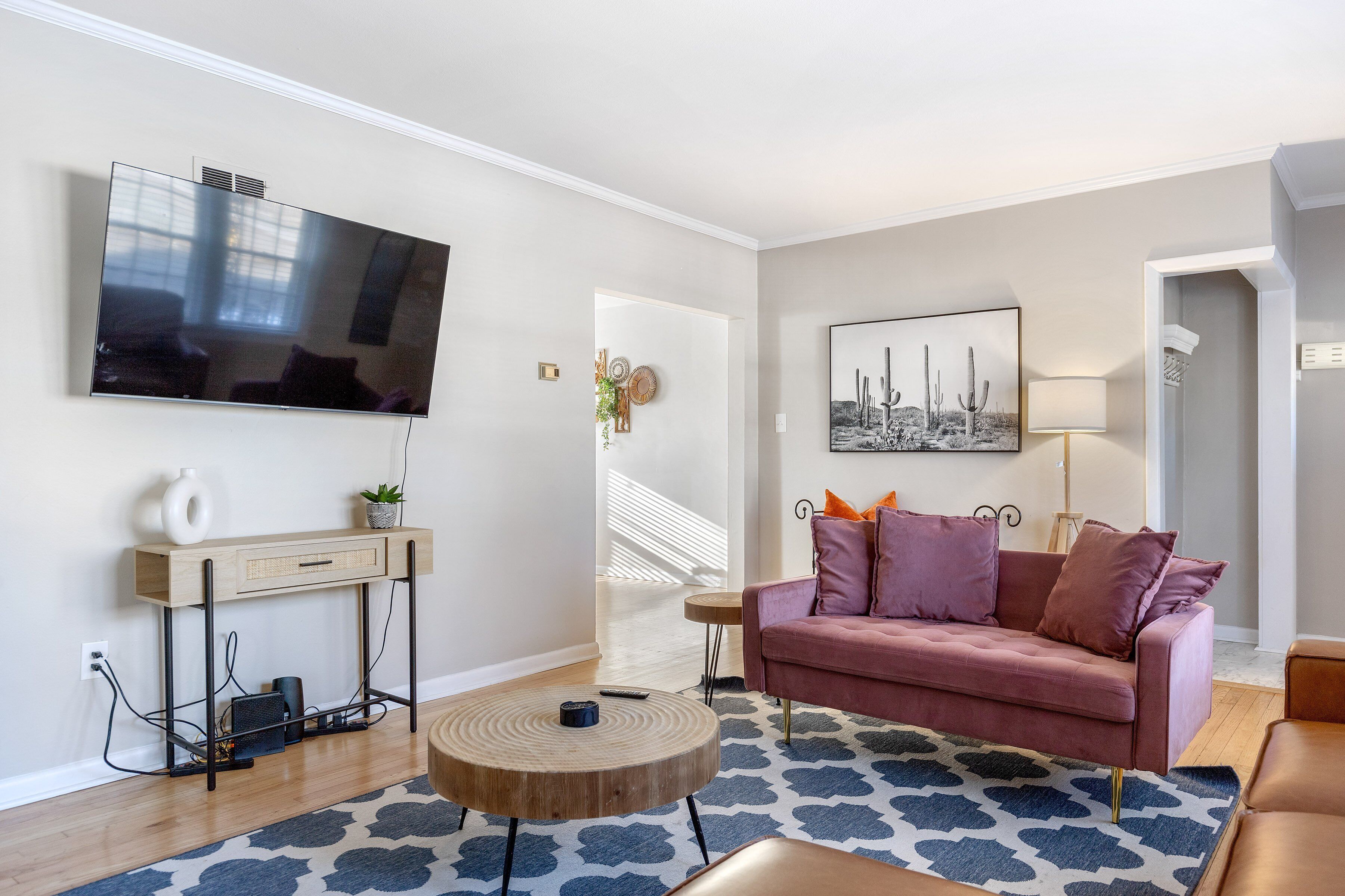 A modern living room with a flat-screen TV, a wooden console table, a round coffee table, a pink sofa, and a patterned rug.