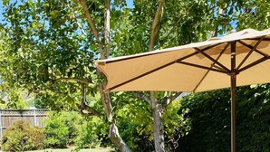 Une terrasse extérieure avec une table et des chaises sous une pergola, entourée de verdure et bordée de briques.