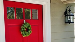 Une porte rouge ornée d’une guirlande verte, une boîte aux lettres et une lanterne fixée au mur.