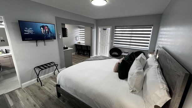 Quarto moderno com uma cama grande, televisão na parede e um banheiro visível através de uma porta aberta.