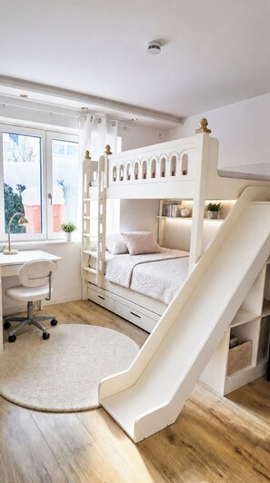 Una cameretta per bambini con un letto a castello, una scrivania, una sedia e una piccola libreria.