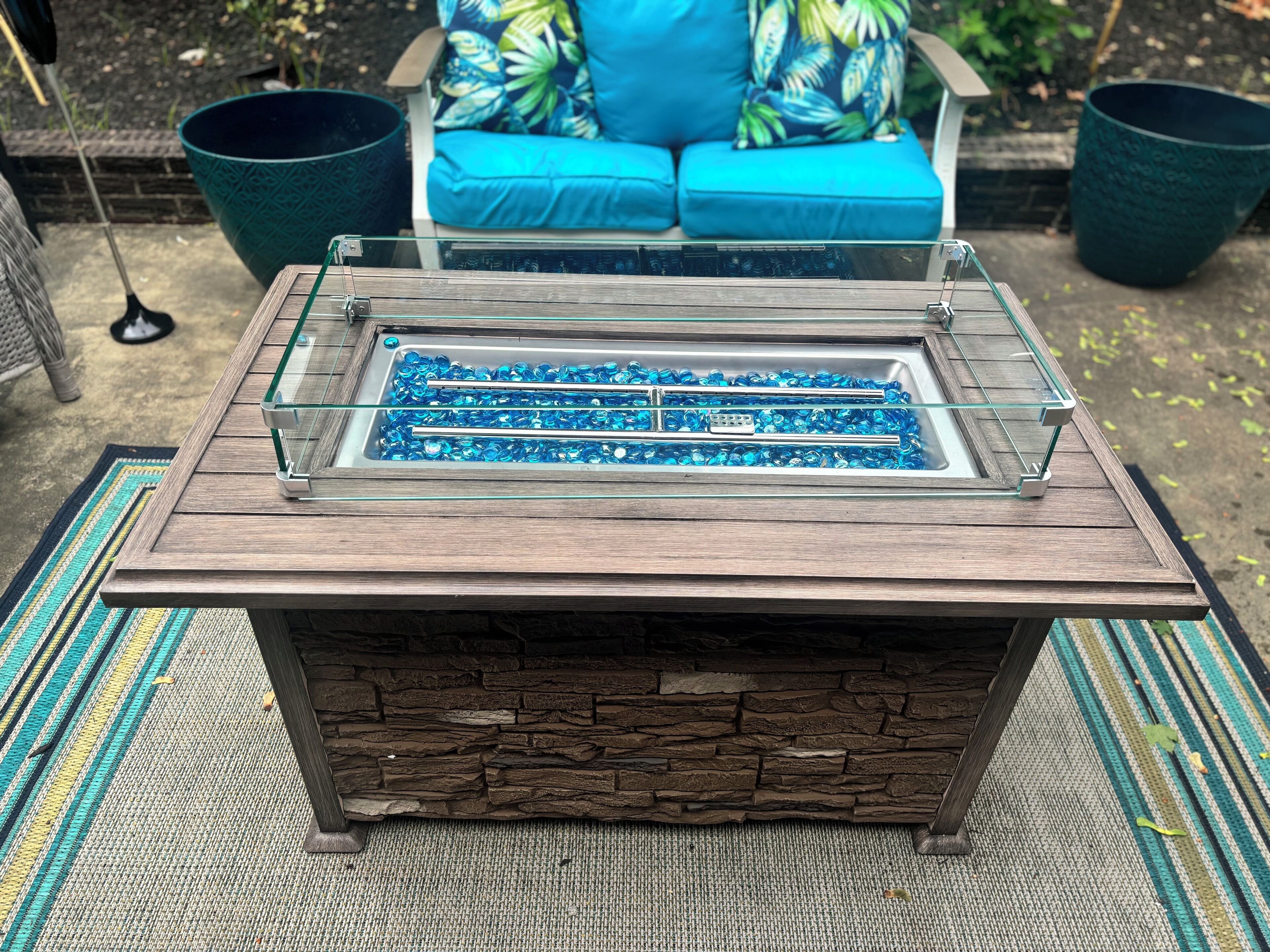A rectangular stone fireplace with a glass top and blue glass pebbles.