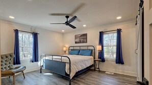 A bedroom with a bed, a chair, a ceiling fan, and two windows with curtains. - Newly Renovated Ranch Overlooking Active Pasture (Clarkesville)