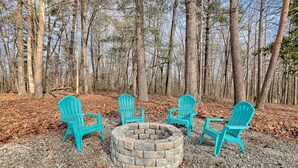 A circular stone fire pit surrounded by four turquoise Adirondack chairs in a forest setting. - Newly Renovated Ranch Overlooking Active Pasture (Clarkesville)