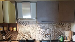 Et moderne køkken med mørke skabe, komfur i rustfrit stål, indbygget ovn og en backsplash med blad-mønster.
