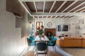 A dining area with a wooden ceiling, a dining table with chairs, a TV, and a sofa.