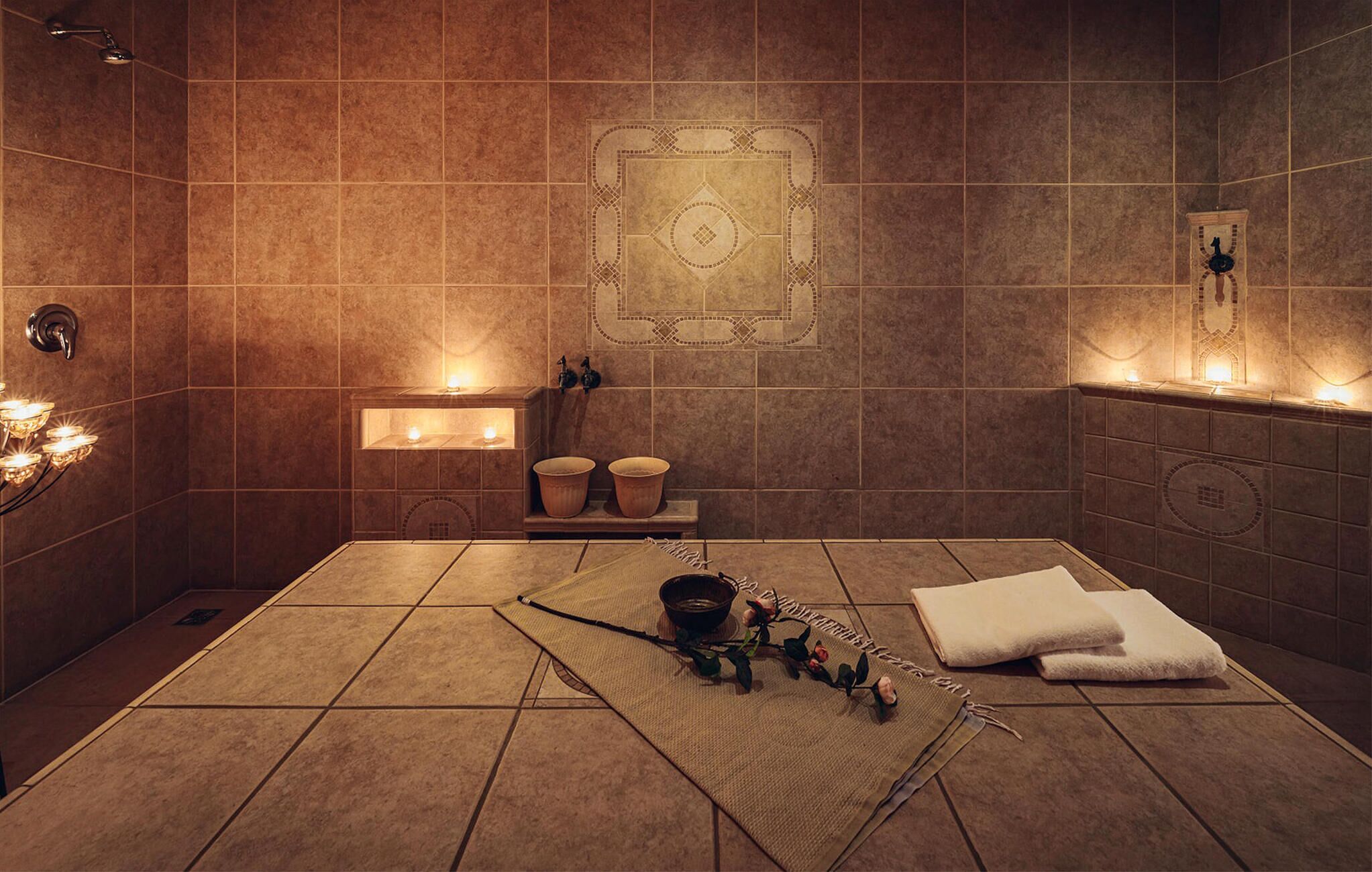 Un baño moderno con una bañera grande, zona de ducha y tocador con espejo. Velas que crean una iluminación ambiental y un diseño decorativo de azulejos en las paredes.