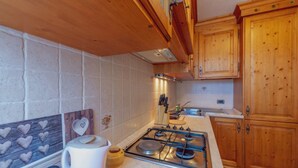 A kitchen with wooden cabinets, a gas stove, and a tiled backsplash. -  CHALET PONTAL 5 - Relax with a beautiful view of the mountains (Courmayeur)