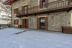 A stone building with a balcony, wooden shutters, and a snow-covered ground.