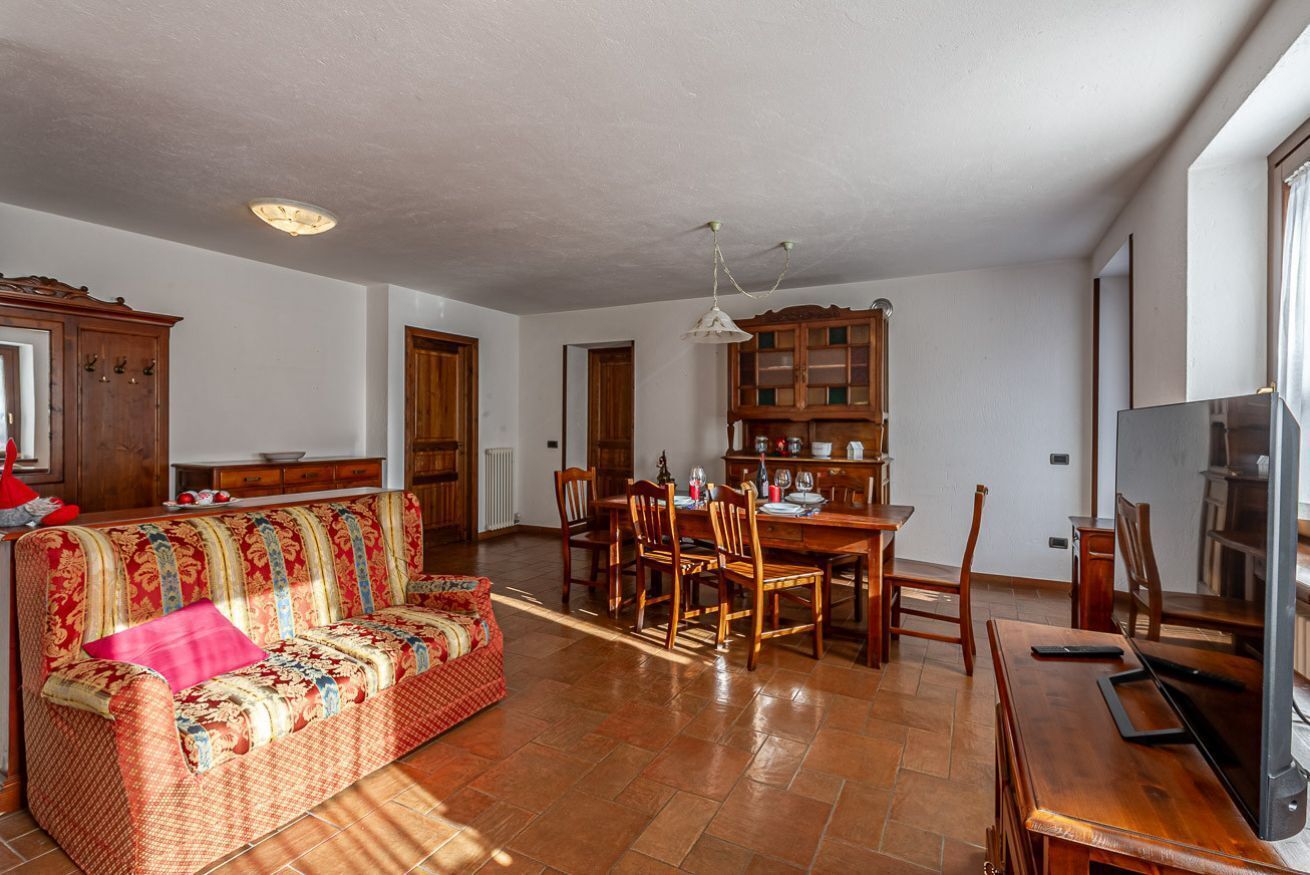 A spacious living area with a sofa, dining table, chairs, and a TV.
